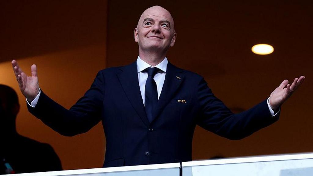 Gianni Infantino smiling with open arms while wearing a FIFA jacket